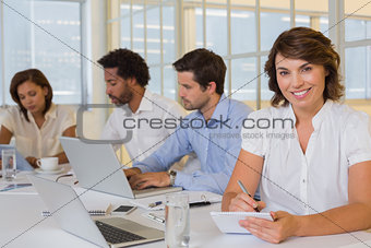 Smiling businesswoman writing notes with colleagues in meeting at office