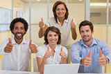 Happy business people gesturing thumbs up at office
