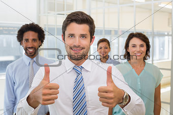 Businessman with colleagues gesturing thumbs up in office