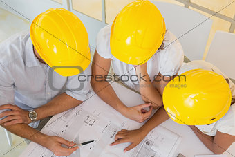 Architects in yellow helmets working on blueprints at office