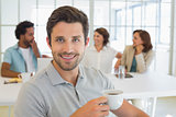 Smiling businessman having coffee with colleagues in background