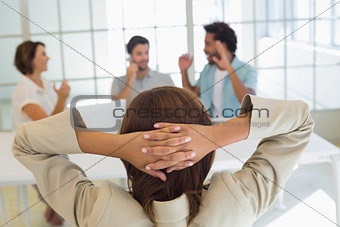Rear view of relaxed businesswoman with colleagues in meeting in background at office