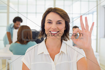 Smiling businesswoman gesturing ok sign with colleagues in meeting