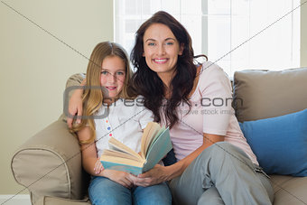 Mother and daughter holding book on sofa