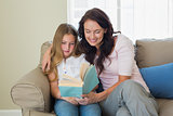 Mother and daughter reading book on sofa