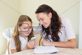 Girl with mother using cell phone at table