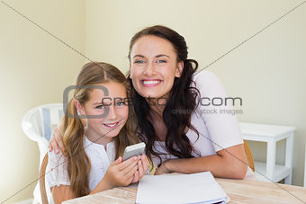 Smiling mother and holding mobile phone at table