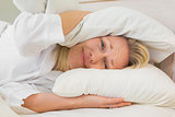 Irritated woman covering ears with pillows