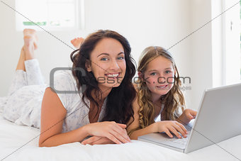 Mother and daughter with laptop lying in bed