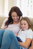 Woman and daughter using tablet computer on sofa