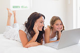 Mother and daughter using laptop in bed
