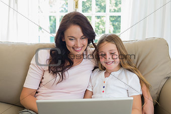 Mother and daughter using laptop together on sofa