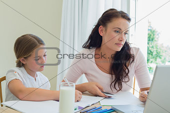 Woman using technologies while daughter studying at table