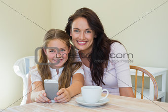 Woman and daughter holding mobile phone at table
