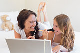 Mother and daughter with laptop applying makeup