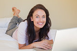 Happy woman with laptop lying in bed