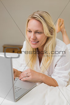 Blond woman using laptop in bed