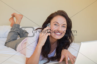 Woman with laptop using mobile phone in bed