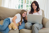 Mother using laptop by daughter on sofa