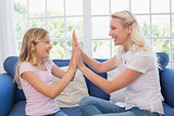 Happy mother and daughter playing clapping game on sofa