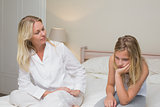 Woman looking at sad girl sitting on bed