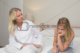 Woman looking at sad girl sitting on bed