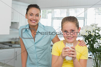 Girl having milk while mother standing by in kitchen