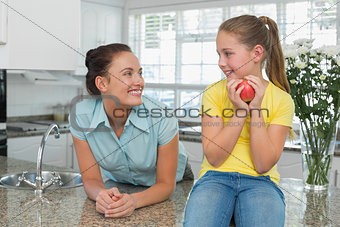 Woman looking at daughter holding apple in kitchen