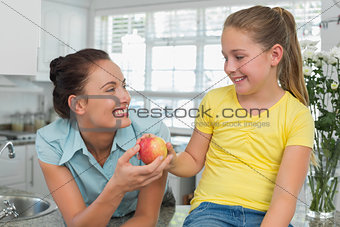 Girl giving apple to mother in kitchen