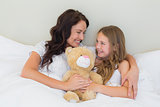Mother and daughter with teddy bear in bed
