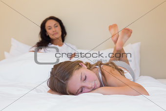 Girl sleeping in bed with mother in background