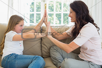 Mother and daughter with hands together on sofa