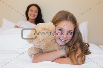 Girl embracing teddy bear with mother in background
