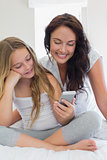 Mother and daughter using mobile phone in bed
