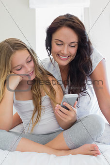 Mother and daughter using mobile phone in bed
