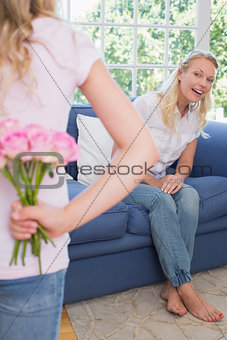 Mother looking at girl hiding flowers behind back