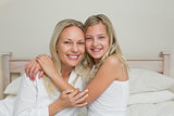 Happy daughter embracing mother in bed