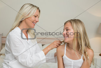 Mother combing hair of daughter in bed