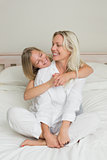 Girl embracing mother sitting in bed