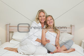 Portrait of mother and daughter sitting in bed