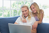 Mother and daughter using laptop on sofa