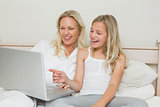 Mother and daughter using laptop together in bed
