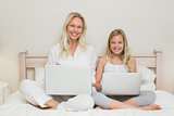 Happy mother and daughter using laptops in bed