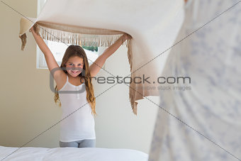 Happy little girl making bed with mother