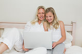 Smiling mother and daughter using laptop in bed