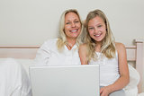 Blond mother and daughter using laptop in bed