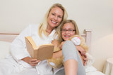 Happy mother and daughter with novel in bed