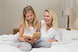Woman looking at daughter reading novel in bed
