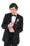 Handsome groom in tuxedo adjusting cuff link