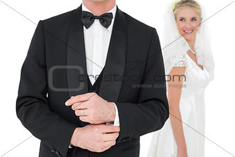 Groom adjusting tuxedo sleeve while bride looking at him